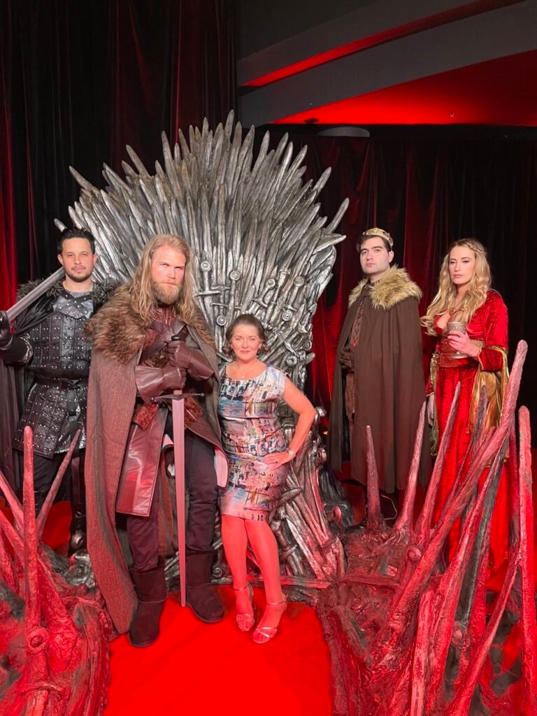 Sarah Monahan and characters from House of the Dragon, sitting on the Iron Throne from Game of Thrones